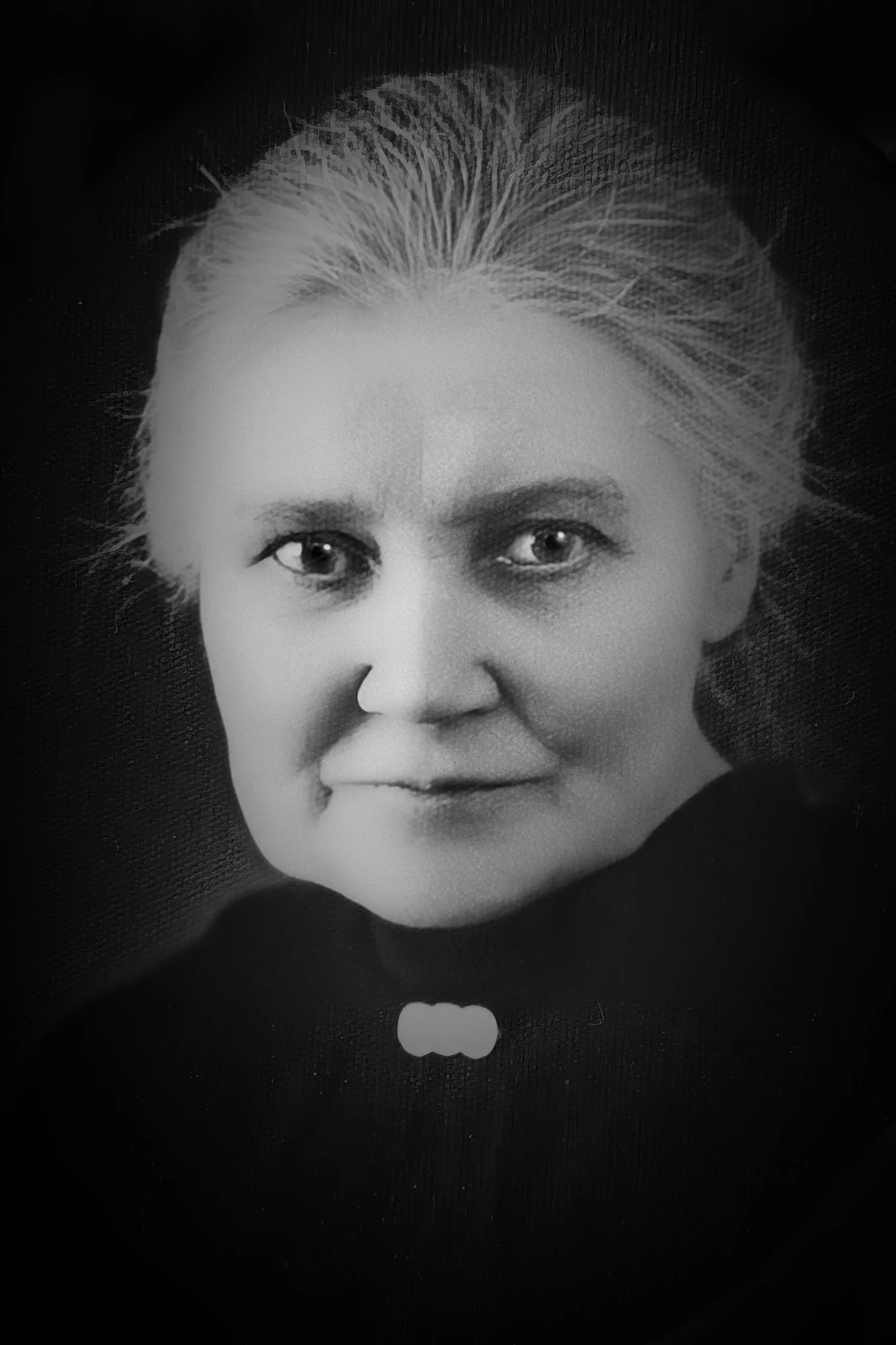 A woman of about 75, with a determined look, in a black dress with three lyres