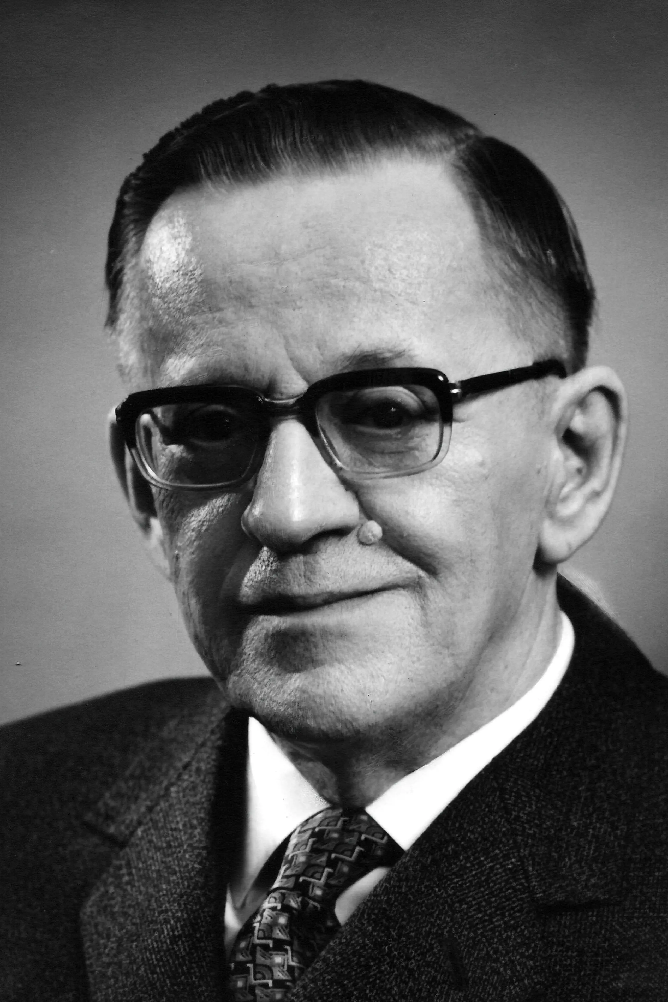 A black-and-white photograph of a 65 years old man wearing glasses