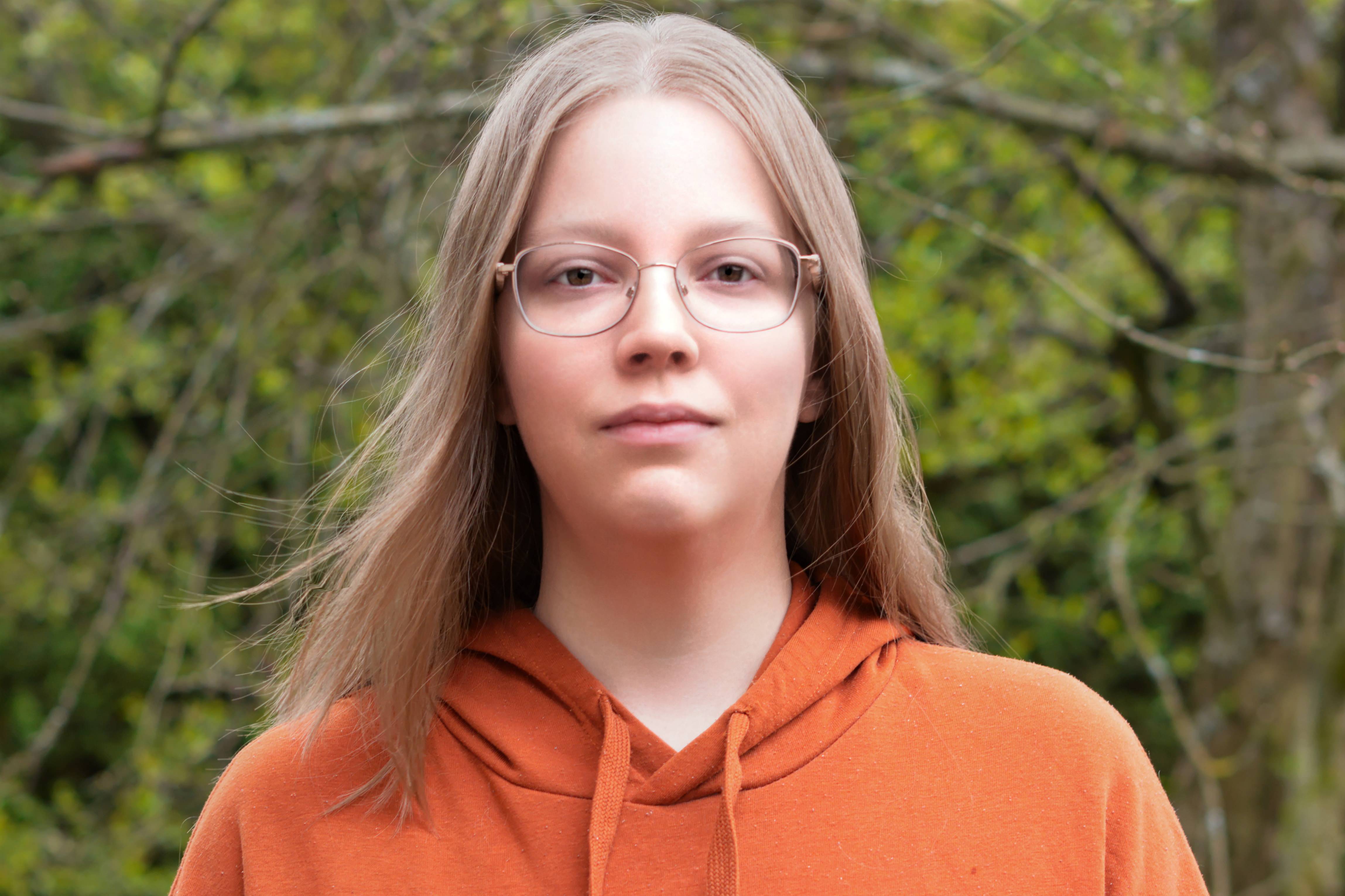 A smart-looking young woman with glasses in an outside garden.